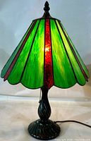 Front view of the stained glass parasol-shaped lamp lit, showing vibrant green and red glass panels with cast metal base.