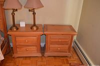 Two matching wooden night tables placed side by side showing the front with two drawers each, round wooden knobs, and natural wood finish.