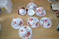 Top-down photo of 8 tea cups and saucers arranged on a table, showing various floral patterns and designs on the china.