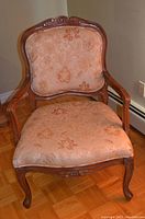 Front view of vintage upholstered arm chair with carved wooden frame and floral fabric upholstery on seat and backrest.