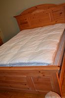 Full view of bed frame including headboard and footboard with mattress topper in place, wood grain visible with natural finish.