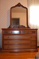 Frontal view of the wooden dresser with mirror showing drawer arrangement and ornate carved details on mirror frame and top of dresser.