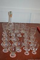 Photo showing the full set of etched glasses and the etched glass decanter bottle with cork stopper arranged on a wooden table.