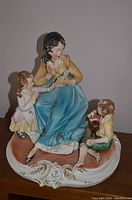 Full view of three-figure Capodimonte porcelain figurine featuring a woman reading to two children seated on detailed base.