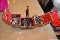 Wood jewellery box with fold-out compartments fully opened, showing various jewellery items inside on red fabric lining.