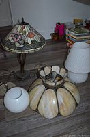 Photo showing three lamps and light fixtures on floor, including stained glass floral lamp, white glass lamp with fabric shade, and large pumpkin-shaped light fixture.