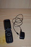 Front view of LG flip phone open with keypad visible and charger plug attached.