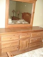Front view of wooden dresser with 9 drawers and central cabinet door topped with large framed mirror.