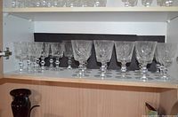 Shelf displaying a row of various sizes of clear crystal glasses with etched pin wheel designs.