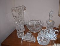 Photo showing the full set of pinwheel crystal water jug, bowl, napkin holder, vase, candy dish, cream and sugar with dish, and decanter on a table.