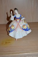 Full front view of the Royal Doulton Christine figurine on wooden shelf.