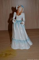 Front angle view of Royal Doulton Emily figurine showing white and blue dress, hat, and woman's red hair.
