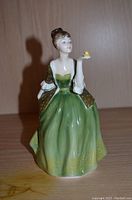 Front view of the Royal Doulton Fleur figurine showing the painted green dress and woman holding a yellow bird.