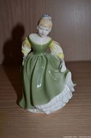 Porcelain figurine of a woman in a green and yellow dress, seated pose, shown close-up.