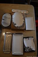 Photo showing seven assorted serving dishes laid out on a table including white ceramic and metal trays with varied shapes and decorative elements