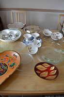 Various serving dishes and trays displayed on table including clear glass bowls, ceramic bowls with floral patterns, covered serving dish, and decorative trays