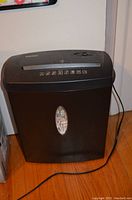 Staples black shredder standing on wooden floor, visible shredded paper through window