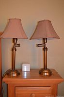 Front view of the pair of brass table lamps with beige fabric shades placed side by side on wooden surface.