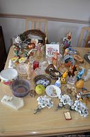 Photo of various trinkets arranged on a wooden table, showing ceramic roses, figurines, plates, and glassware.