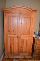 Front view of the wooden wardrobe/entertainment unit showing double doors with decorative carving on top and round wooden knobs.
