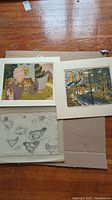 Overview of three artworks laid out on floor: boats woodcut, floral print and chicken sketch page