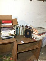 Wide view showing multiple stacks and a box of art-related books mostly about ships and maritime themes on wooden shelving units.