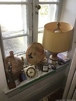 Overview showing marble base lamp with yellow shade, pottery jug, brass candle holders, small clocks, decorative tray with pheasant, glass paperweight, and table linens basket.