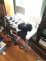 Two white shower chairs with metal legs and sliding rails in a room, showing straps and rails on the floor.