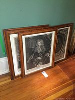 Three framed black and white engraved portraits leaning on floor against wall, showing wood frames and mat borders.