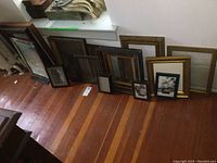 Collection of multiple picture frames and one mirror arranged on a wooden floor, showing variety in sizes and styles.