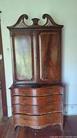 Front view of wood secretary cabinet with decorative top, four curved drawers, and two cabinet doors.