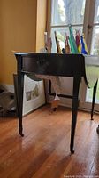 Photo shows side view of small dark wood drop leaf table with drawer under top surface and several colorful glass sailboat figurines on top.
