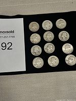 Top view showing all twelve Washington silver quarters laid out in rows on a black cloth background.