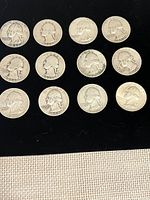 Front view of 12 Washington quarters arranged in rows on black surface showing obverse side with Liberty and dates visible.