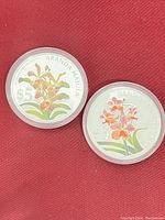 Two silver proof coins with colorful orchid engravings on front.