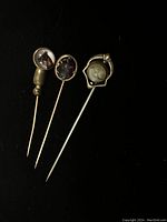 Three vintage lapel pins with distinct designs on black background showing details of pins' heads and shafts.