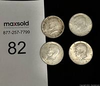 Four Kennedy half dollars displayed on black and white background with visible coin details and dates.
