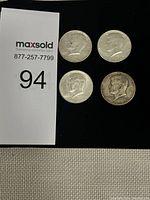 Four Kennedy Half Dollar coins with a MaxSold auction tag. Coins all show obverse side with Kennedy's profile.