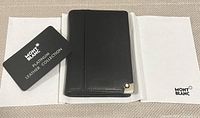 Closed view of the black Montblanc Blanc compact leather wallet alongside Montblanc certificate card and branded cloth.