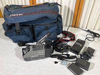 Full kit laid out including JVC VHS camera, 3 batteries, charger, cables, and blue Tamrac camera bag with multiple compartments.