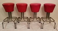 Four red vinyl mid-century modern barstools with chrome legs arranged in a row against a wall showing full front view.