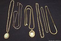 All six gold-tone chains and two lockets displayed on black background showing variety of chain link styles and lockets.