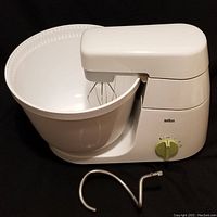 Side view of Braun KM32 mixer assembled on white plastic mixing bowl, wire beaters installed, and metal dough hook attachment placed in front