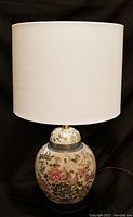 Full view of the lamp showing the cream-colored ginger jar base with floral pattern and white drum lampshade.