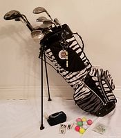 Photo showing used zebra print Cutler golf bag standing with golf clubs inside, accessories laid out including golf balls and black pouch