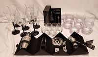Wine glasses with black stems, old-fashioned and liqueur glasses with bubble bottoms, Danesco bar set, and Mafiti aerator in box arranged on white cloth.