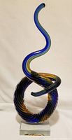 Full front view of Murano glass sculpture showing twisting circular base and spiraled tall neck in blue and yellow hues, mounted on clear square base.