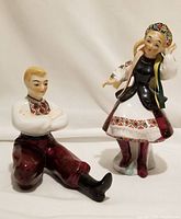 Front view of seated male and standing female ceramic Ukrainian dancer figurines with detailed handpainted clothing.