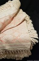 Close-up of the silver pink jacquard pattern and fringed edge of the bedspread, showing detailed ornate weaving and texture.