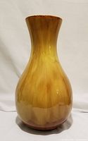 Front view of a tall ceramic vase in harvest gold and brown glaze on white background.